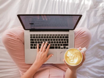 Woman on her laptop shopping for candles while drinking a latte. 